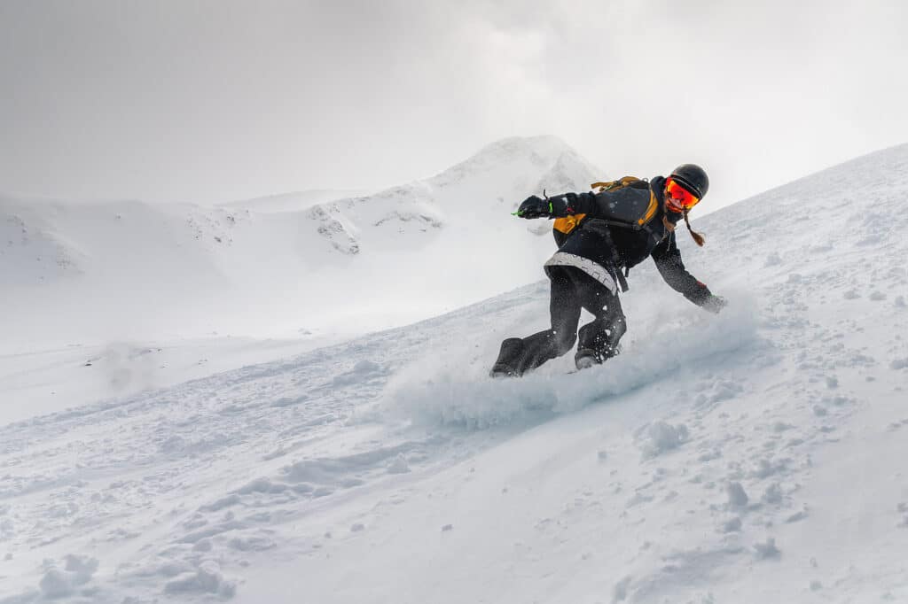 Snowboarder, a young woman in motion on a snowboard in the mountains in a freeride not far from the ski slope, makes a downhill skiing